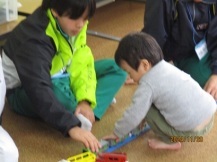 幼児と中学生がプラレールで遊んでいる写真