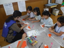 折り紙の作り方をスタッフに教わる児童の写真