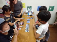 職員にカードゲームのやり方を教わる小学生児童の写真