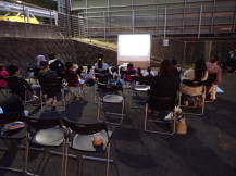 こども文化センターの庭で夜間の映画上映会に参加する来館者の写真