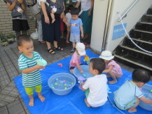 水の入ったたらいの周りで遊ぶ幼児の写真