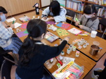 布きんちゃくにスタンプを押したりイラストを描いたりする小学生児童の写真