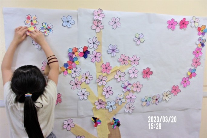 桜の花のぬりえを木に貼り付ける子どもたちの写真